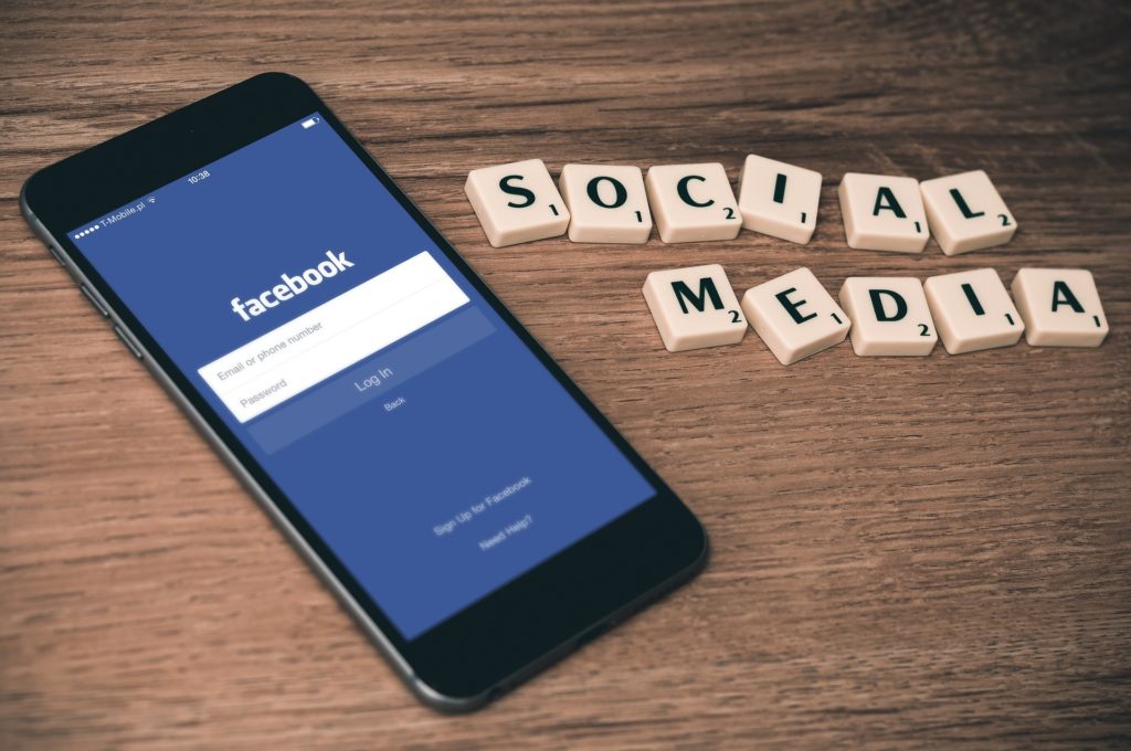 Cette photo provenant de Pixabay, Firmbee, Social Media montre un smarthphone avec l'application Facebook en cours d'ouverture et des lettres issues du jeu Scrabble formant deux mots : "social media"